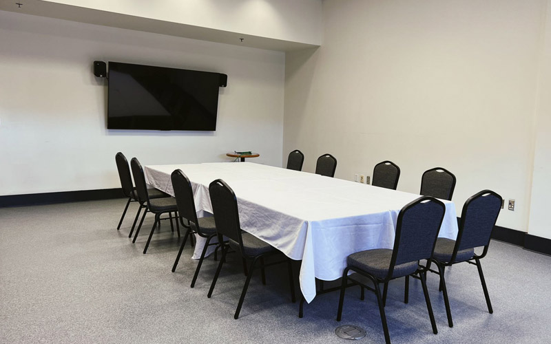 A small room with tall ceilings set with a large boardroom table for eight guests, and a TV with two speakers for presentations.