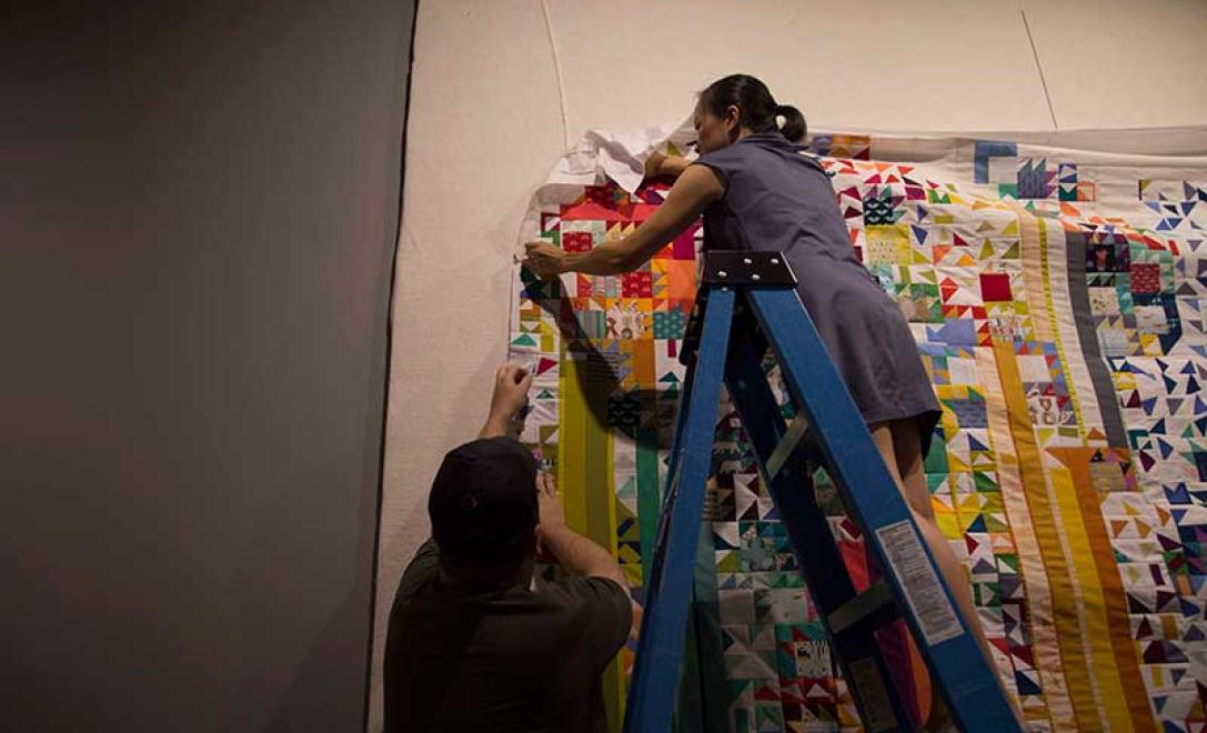 A woman can be seen trying to hang a quilt on the wall.