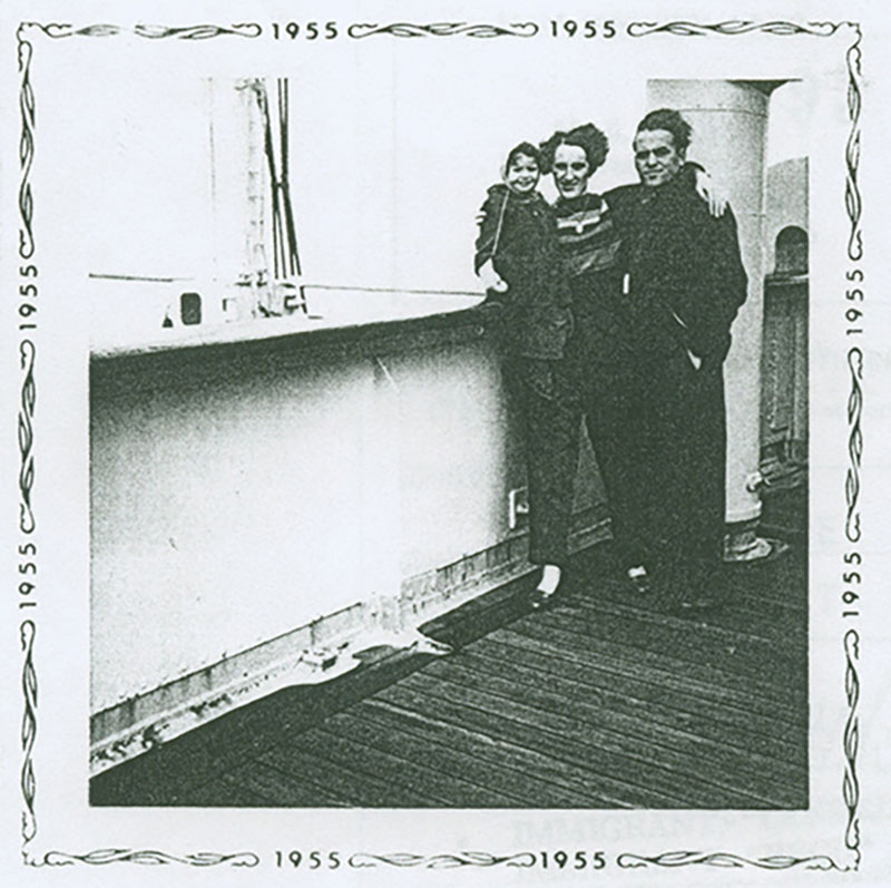 Archival photo dated 1955 showing a ship’s deck with a woman, man and child. The woman is in the middle and has each arm around the child and man.