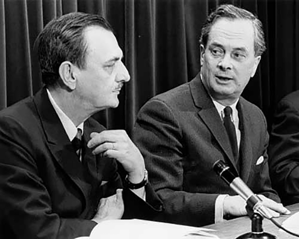 Archival photo of two men in suits sitting in front of a microphone.