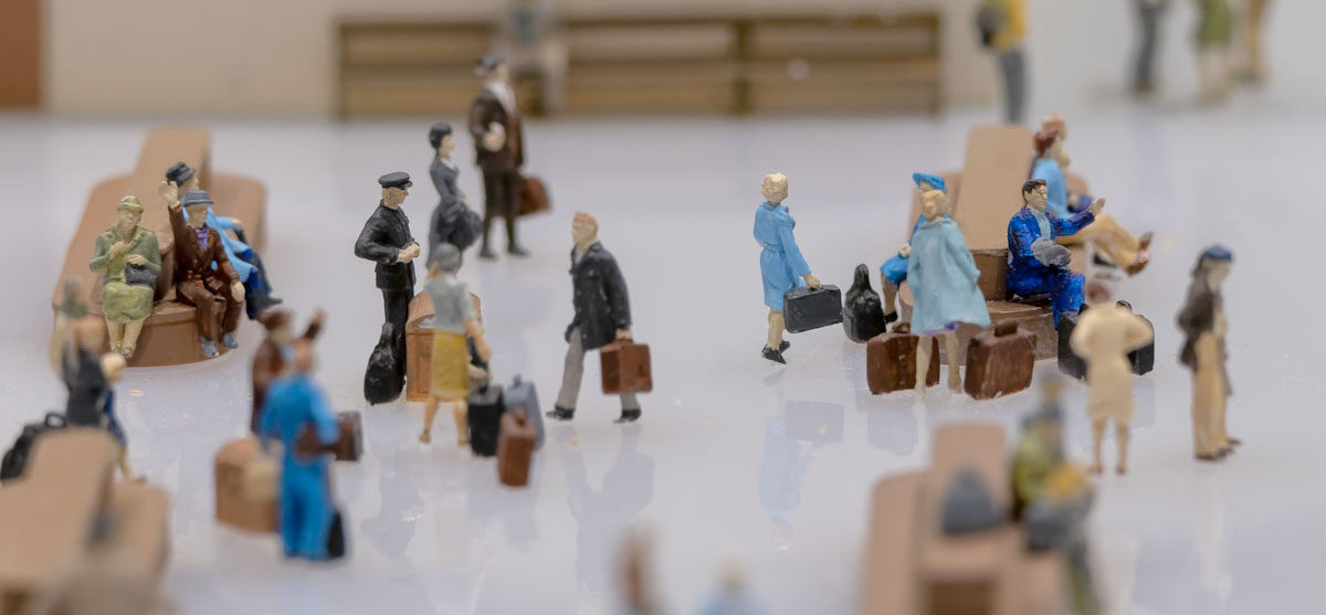A model of a waiting room with a few dozen light-skinned people and their luggage.