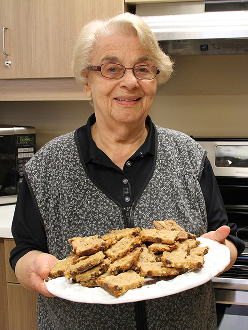 Une vieille dame souriante tient un plat de biscuits fraîchement cuits et les tient à la caméra.