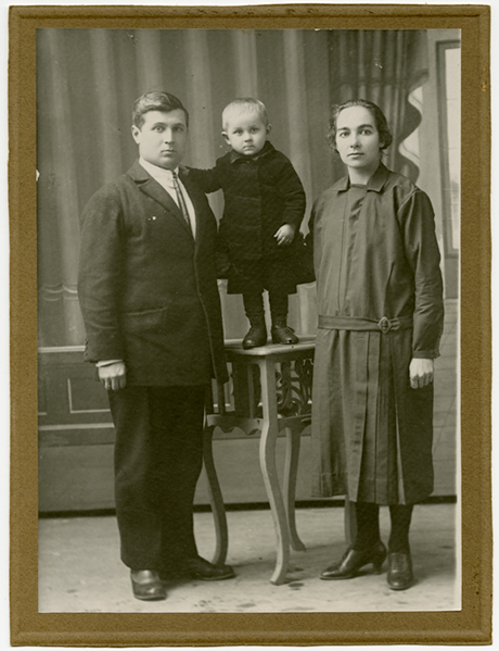Archival black and white photo of a couple with their little son standing on a table.