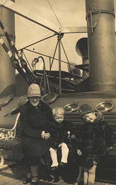 A young woman sits with a baby in her lap while a little girl stands next to her.