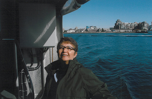 A woman stands on the deck of a ferry, blue water in the background.