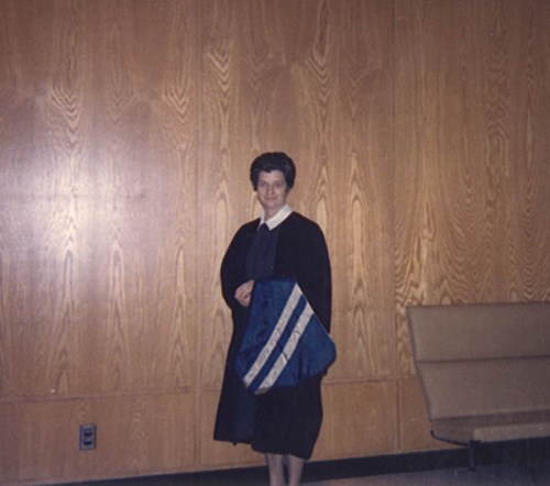 Young lady wearing black dress standing in front of wooden wall.