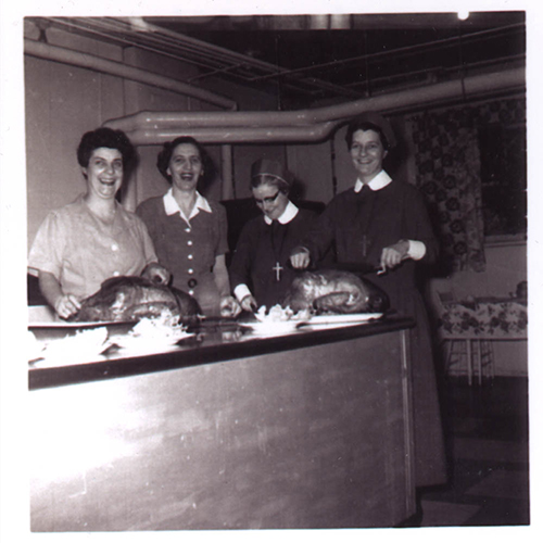 Group of four ladies standing behind kitchen counter.