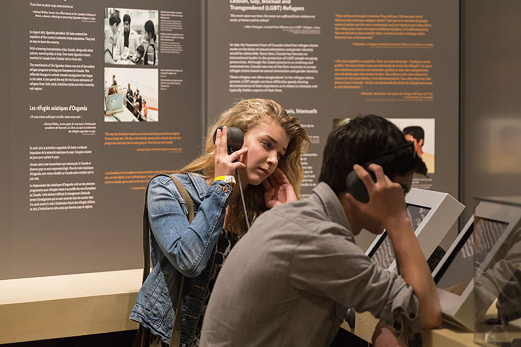 A young boy and girl listen to head phones which tell the story of a refugee.