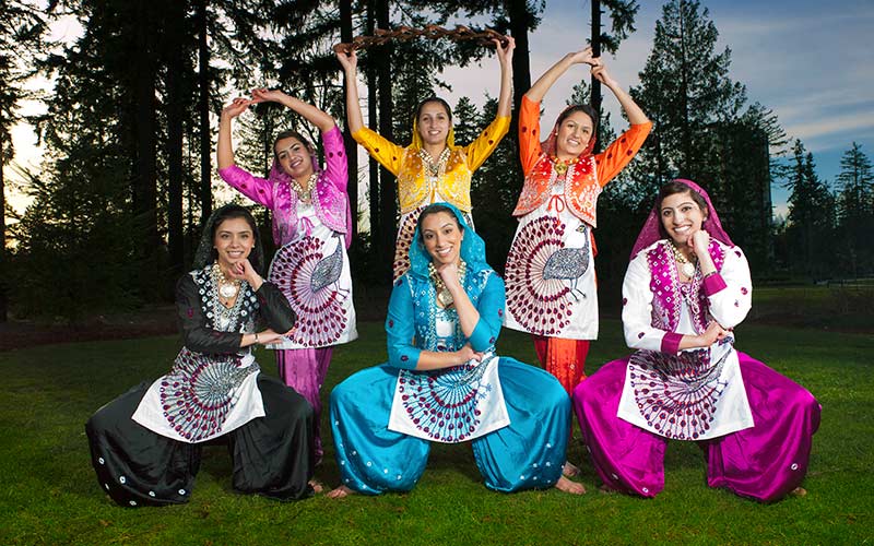 Six female Bhangra dancers pose in cultural dress.
