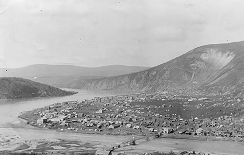 A large settlement sits at the base of a mountain next to a river.