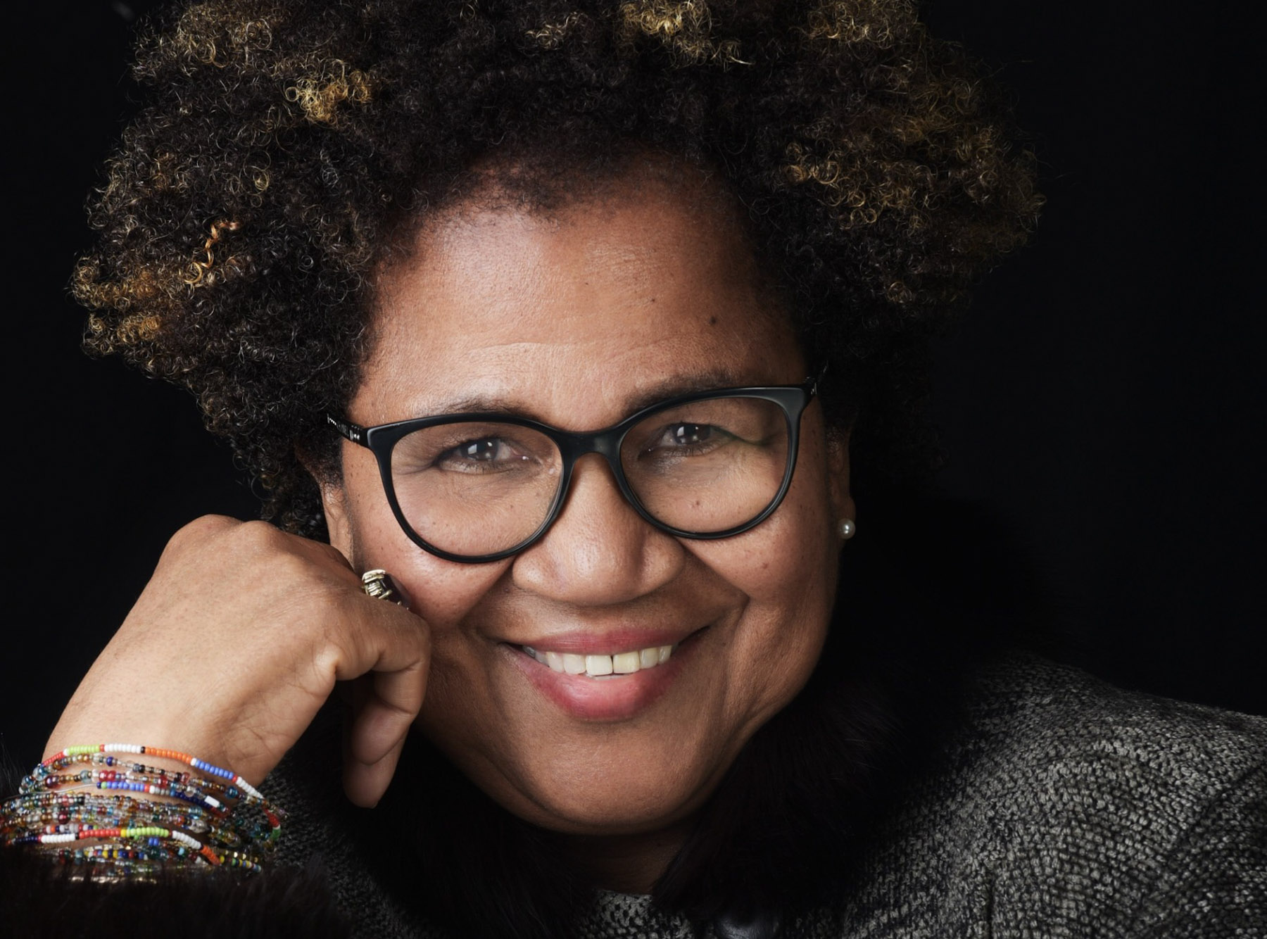 Portrait of Joy Bullen, a smiling dark-skinned woman with glasses.