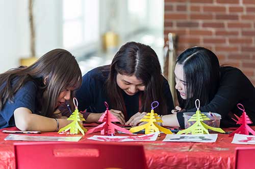 Three young ladies are at a table, doing crafts.