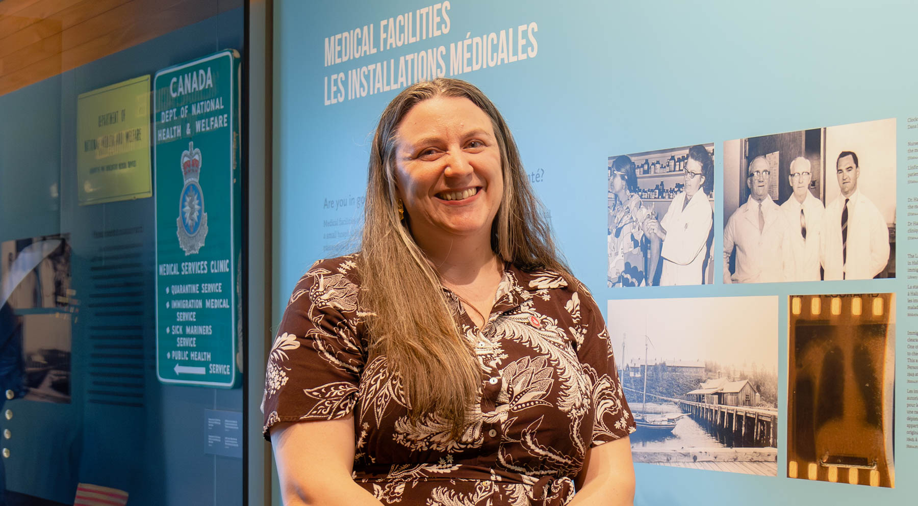 A middle-aged white woman with long hair smiles next to a black and white photo of three doctors.