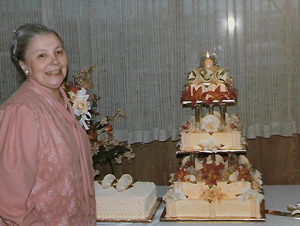 A young woman stands next to a cake she made.