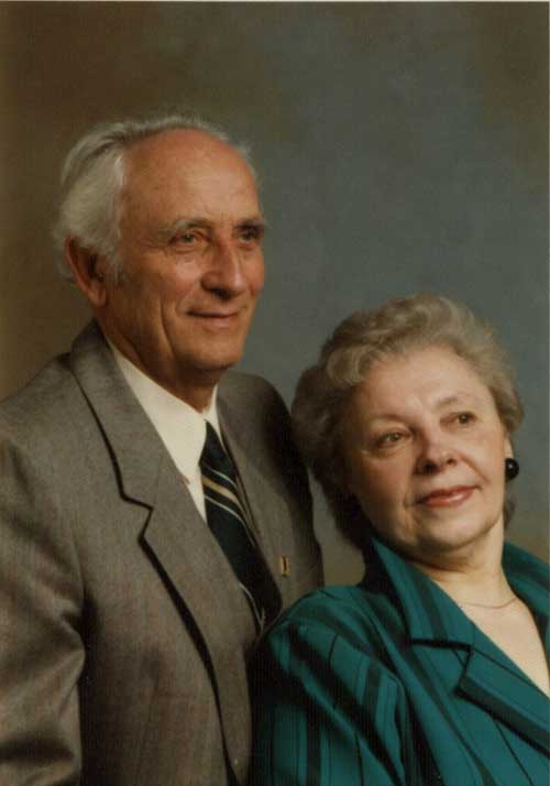 An anniversary portrait with the man standing behind a woman who is seated.
