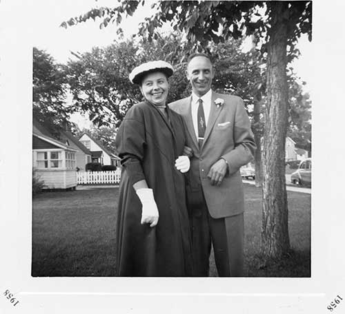Old black and white photo of smiling couple by a tree.